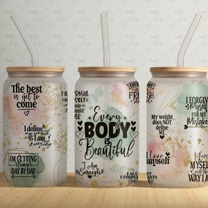 May include: Three frosted glass tumblers with bamboo lids and clear straws. Each tumbler features inspirational quotes and floral designs in gold, pink, and green. The text includes phrases like "Every Body is Beautiful" and "I love myself."