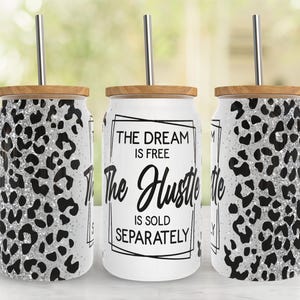Könnte beinhalten: Drei Glasbecher mit Bambusdeckeln und Edelstahlstrohhalmen. Die Becher haben einen weißen Hintergrund mit einem schwarzen und silbernen Leopardenmuster. Ein Becher hat den Text "THE DREAM IS FREE The Hustle IS SOLD SEPARATELY".