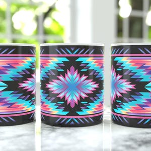 May include: Three white ceramic mugs with a vibrant, geometric pattern in shades of pink, purple, turquoise, and black. The design features a central starburst motif and repeating chevron shapes, creating a colorful and eye-catching design.