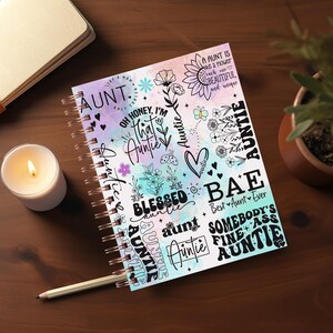 May include: A colorful spiral bound notebook with a watercolor background and black text that says "AUNT" and other phrases like "Oh honey, I'm that auntie", "Blessed auntie", "Bae Best Aunt Ever", "Somebody's Fine Ass Auntie".