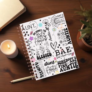 May include: A white spiral bound notebook with a colorful design featuring the word "Auntie" in various fonts and styles. The design also includes flowers, hearts, and other decorative elements.
