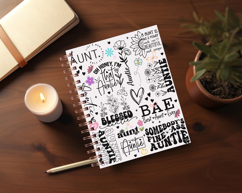 May include: A white spiral bound notebook with a colorful design featuring the word "Auntie" in various fonts and styles. The design also includes flowers, hearts, and other decorative elements.