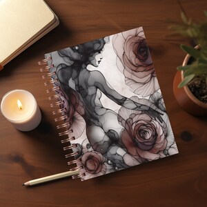 May include: A spiral bound journal with a black and white illustration of a woman with a floral design in shades of pink and gray.