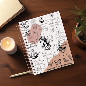Może przedstawiać: Biały notes w spirali z różowo-czarnym wzorem. Okładka zawiera inspirujące cytaty i ilustracje, w tym motyle, pióra i półksiężyc. Tekst na okładce zawiera takie frazy jak "Stwórz przestrzeń, aby być szczęśliwym", "Spokojny umysł może poradzić sobie z każdą burzą" i "Różne jest piękne".