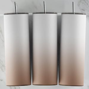 May include: Three stainless steel tumblers with a gradient design. The tumblers are white at the top and fade to a light brown at the bottom.