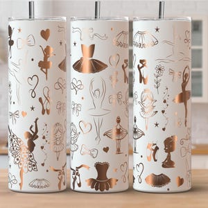 May include: Three white insulated tumblers with a ballet theme. Each tumbler features a repeating pattern of ballet dancers, tutus, hearts, and bows in a rose gold color. The tumblers have a silver straw and lid.