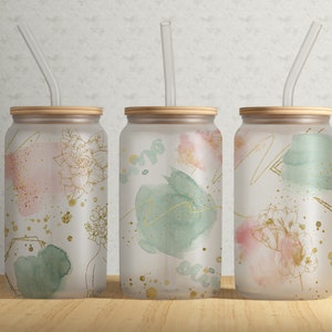 Peut inclure: Trois gobelets en verre givré avec des couvercles en bambou et des pailles transparentes assorties. Chaque gobelet présente un motif abstrait différent avec des lavis de rose, de vert et d'or rappelant l'aquarelle, et des accents en feuille d'or.