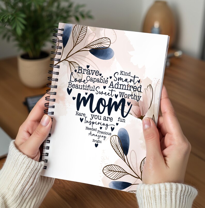 May include: A spiral-bound notebook with a floral design and the word "Mom" in the center. The notebook's cover features the words "Brave, Love, Capable, Beautiful, Sweet, Rare, Inspiring, Needed, Precious, Amazing, Bright, Kind, Smart, Admired, Worthy, You are fun".