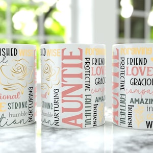 May include: Three white ceramic mugs with various words printed on them, including "AUNTIE", "CHERISHED", and "LOVED". The mugs have a floral design and are in a row on a marble surface.