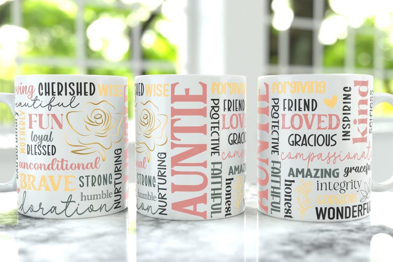 May include: Three white ceramic mugs with various words printed on them, including "AUNTIE", "CHERISHED", and "LOVED". The mugs have a floral design and are in a row on a marble surface.