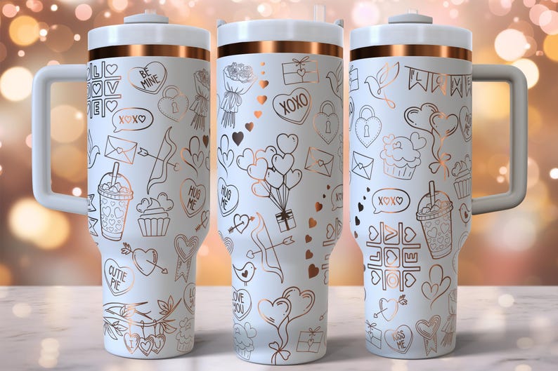 K&ouml;nnte beinhalten: Drei wei&szlig;e Edelstahlbecher mit ros&eacute;goldenen Akzenten und verschiedenen Designs zum Valentinstag. Die Designs beinhalten Herzen, Pfeile, Cupcakes und die Worte "Be Mine", "XOXO", "Hug Me" und "Cutie Pie".