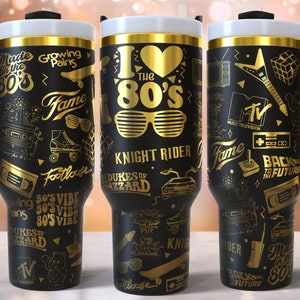 K&ouml;nnte beinhalten: Drei schwarze und goldene Edelstahlbecher mit verschiedenen Grafiken zum Thema der 1980er Jahre, darunter die Worte "I Love the 80's", "Knight Rider", "Zur&uuml;ck in die Zukunft" und "Dukes of Hazzard".