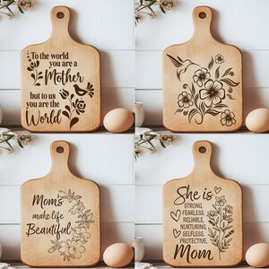 K&ouml;nnte beinhalten: Vier Holzschneidebretter mit eingravierten Designs und Text. Ein Brett tr&auml;gt die Aufschrift "To the world you are a Mother but to us you are the World." Ein anderes zeigt einen Kolibri und Blumen. Ein drittes sagt "Mom's make life Beautiful." Das letzte sagt "She is Mom."