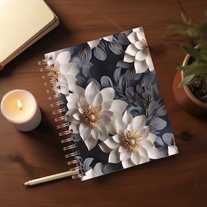 May include: A spiral-bound notebook with a floral design featuring large white flowers with gold centers and gray-blue leaves on a dark background. The notebook is open, and a pencil and lit candle are nearby.