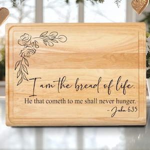 May include: A rectangular wooden cutting board with a decorative floral design in the upper left corner. The text "I am the bread of life. He that cometh to me shall never hunger. -John 6:35" is engraved on the board.