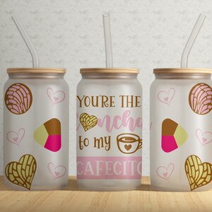 May include: Three frosted glass tumblers with lids and straws. The tumblers have a pink and brown design with hearts and a pastry. The middle tumbler has the text "You're the concha to my cafecito".