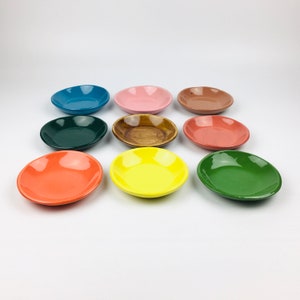 May include: Nine small, oval-shaped ceramic dishes in various colors, including blue, pink, brown, green, orange, and yellow. The dishes are arranged on a white surface, showcasing their vibrant hues and glossy finish. The dishes are ideal for serving small portions.