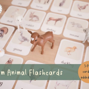 May include: Farm animal flashcards with illustrations and animal figurines. The cards feature images of a duck, rabbit, turkey, goose, donkey, mouse, lamb, and duckling. A brown cow, white lamb, and white chicken figurines are placed on the cards.