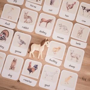 May include: Educational flashcards featuring farm animals, including a duck, rabbit, donkey, and more. A toy horse is placed among the cards. The cards have the animal's name printed below the image. The background is a light brown wooden surface.