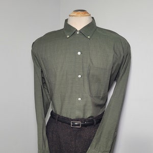 May include: A long-sleeved, green button-down shirt with a black belt. The shirt has a pocket on the left side and a subtle pattern.
