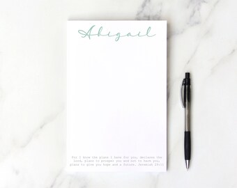 May include: A white notepad with the name "Abigael" written in teal script at the top. The notepad has a quote from Jeremiah 29:11 printed at the bottom. "For I know the plans I have for you, declares the Lord, plans to prosper you and not to harm you, plans to give you hope and a future. Jeremiah 29:11"
