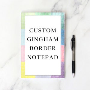 May include: A white notepad with a custom gingham border in shades of green, blue, pink, yellow, and purple. The notepad says "Custom Gingham Border Notepad" in black text.