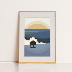 May include: A framed print of a stylized landscape with a black silhouette of a bison in the foreground. The background features a yellow sun, blue and green hills, and a white cloud.