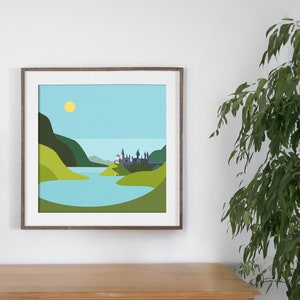 Op de afbeelding: Een ingelijste illustratie van een kasteel met torens, omringd door groene heuvels en een blauw meer. De zon schijnt aan een blauwe hemel.