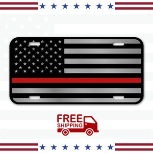May include: A black and silver American flag with a red stripe across the middle. The flag is on a metal license plate.