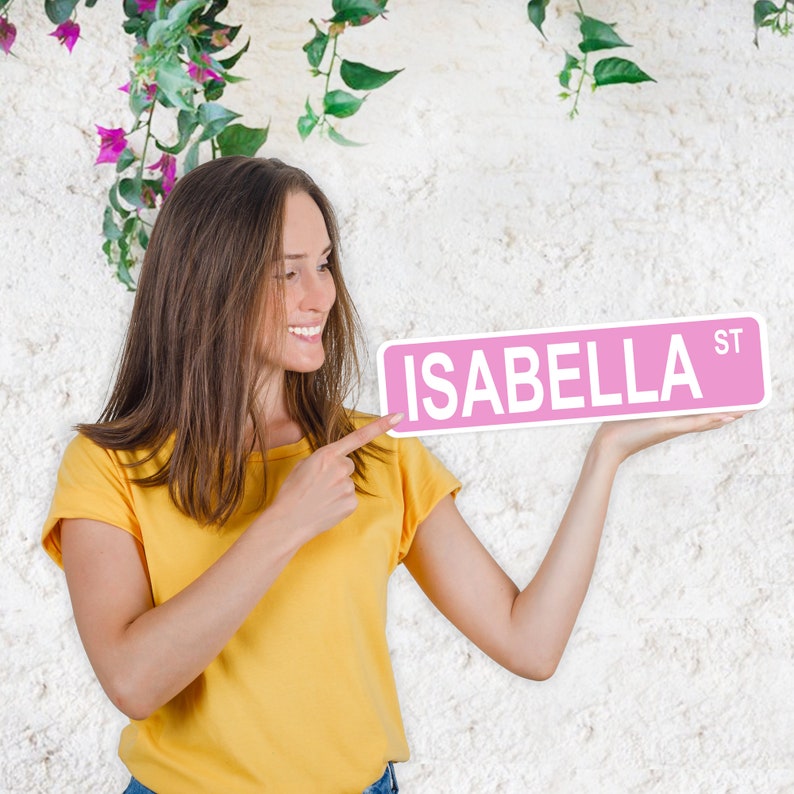 Puede incluir: Una mujer se&ntilde;ala una se&ntilde;al de calle rosa con el nombre "ISABELLA ST" escrito en letras blancas.