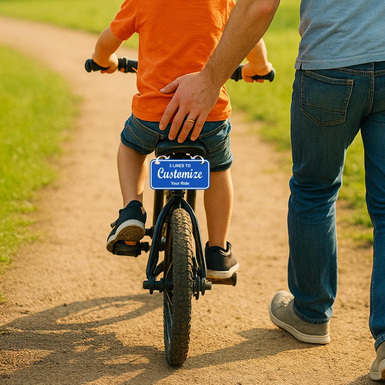 May include: A child in an orange shirt and denim shorts rides a black balance bike on a dirt path, with an adult's hand on the child's back. The bike has a blue plate that says "3 Lines to Customize Your Ride."