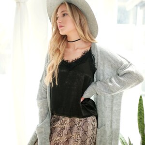 Puede incluir: Una mujer con un c&aacute;rdigan gris, una blusa negra de encaje, una falda de estampado de serpiente, un fedora gris y botas marrones.