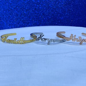 May include: Three gold, silver, and rose gold bracelets with the names "Kamielle", "Karyn", and "Aniya" engraved on them.