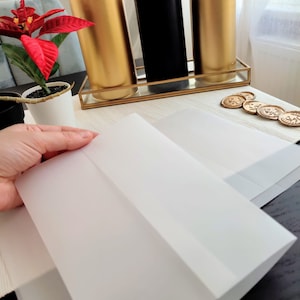 Pu&ograve; includere: Due buste bianche su una superficie nera. Le buste sono piegate a met&agrave; e pronte per essere sigillate. Sullo sfondo ci sono tre candele, una nera e due dorate.