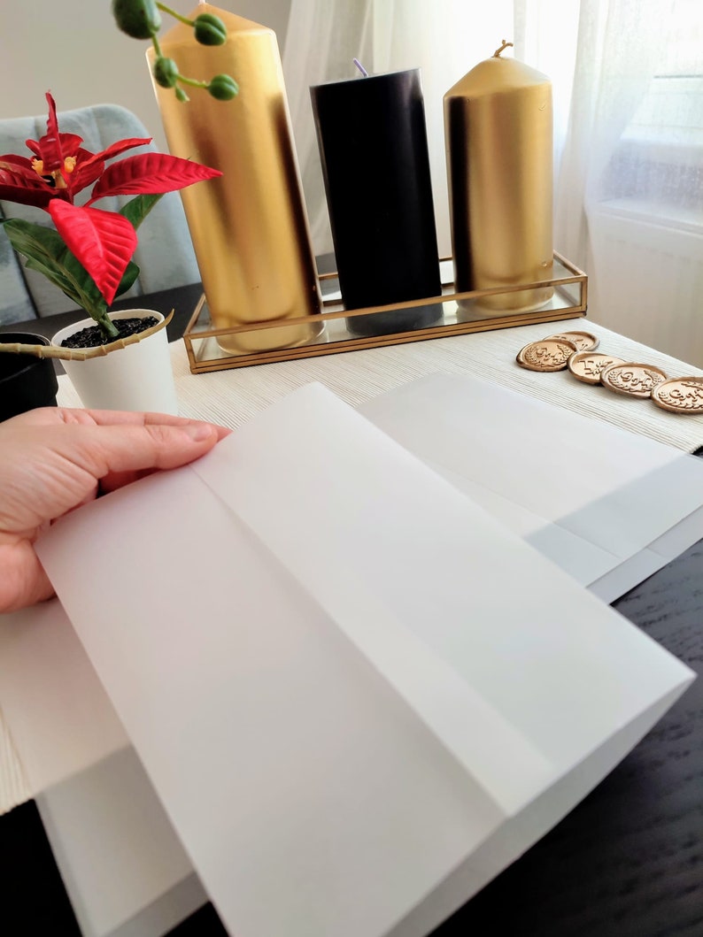 Pu&ograve; includere: Due buste bianche su una superficie nera. Le buste sono piegate a met&agrave; e pronte per essere sigillate. Sullo sfondo ci sono tre candele, una nera e due dorate.