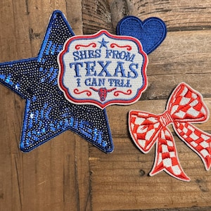 Peut inclure: Un ensemble de quatre écussons brodés comprenant une grande étoile bleu foncé à paillettes, un petit cœur bleu uni, un écusson blanc en forme de blason avec bordure rouge et le texte SHES FROM TEXAS I CAN TELL, et un nœud à carreaux rouge et blanc.