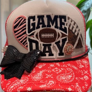 Dunkelrosa-weiße Truckerkappe im Football-Design. Mehrere Aufnäher. Schwarze Paillettenschleife. Strasssteine. Kette. Für Damen und Teenager.