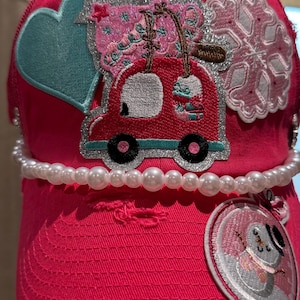 May include: A vibrant pink baseball cap adorned with embroidered patches and a pearl bead band. Patches feature a blue heart, a red car, a pink snowflake, and a snowman. The cap has a distressed brim.