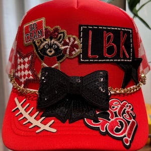 Red and white trucker hat with checkered mesh .   Ladies hat .  Multiple patches.   Raccoon cheerleader.  Lubbock .