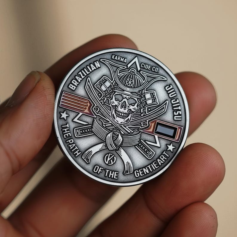 May include: A silver coin featuring a skull wearing a samurai helmet, crossed swords, and the words "Brazilian Jiu Jitsu." The coin also includes the text "The Path of the Gentle Art" and "Karma Cide Co."