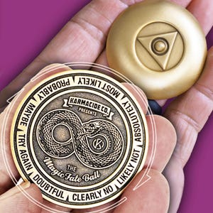 May include: Two gold-coloured metal fortune-telling coins. One coin features a snake design with the text "The Magic Fate Ball" and phrases like "Maybe" and "Absolutely Not." The other coin has a triangle and circle design.
