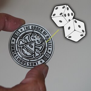 Peut inclure: Une pi&egrave;ce de monnaie en m&eacute;tal argent&eacute;e avec un motif de cr&acirc;ne et d'os crois&eacute;s. La pi&egrave;ce porte l'inscription "The Order of Baleeci" et "Omnia Ludus Sunt" sur le bord. Deux d&eacute;s blancs sont repr&eacute;sent&eacute;s dans le coin sup&eacute;rieur droit de l'image.