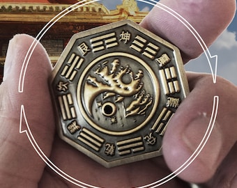 May include: A silver and gold octagonal coin with a yin yang symbol and a tree design. The coin has Chinese characters around the edge.