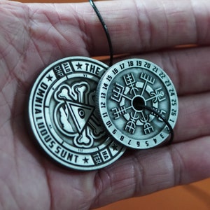 Peut inclure: Deux pendentifs en m&eacute;tal argent&eacute; sur un cordon noir. Le plus grand pendentif pr&eacute;sente un motif de boussole avec des chiffres romains et les mots "ALD CHP" et "THE VI". Le plus petit pendentif pr&eacute;sente un motif de cr&acirc;ne et d'os crois&eacute;s avec les mots "OMNIA LOQUUNTUR HA TER" et "III SSUNT".