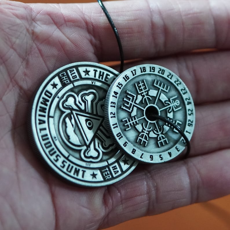 Peut inclure: Deux pendentifs en m&eacute;tal argent&eacute; sur un cordon noir. Le plus grand pendentif pr&eacute;sente un motif de boussole avec des chiffres romains et les mots "ALD CHP" et "THE VI". Le plus petit pendentif pr&eacute;sente un motif de cr&acirc;ne et d'os crois&eacute;s avec les mots "OMNIA LOQUUNTUR HA TER" et "III SSUNT".