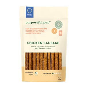 May include: A package of Purposeful Pup Chicken Sausage dog treats. The beige bag features text including "Chicken Sausage" and "Premium Dog Treats." The treats are brown, stick-shaped, and visible through a clear window.