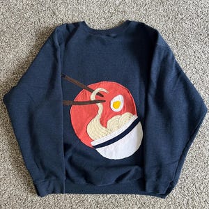 May include: A navy blue sweatshirt with a red, white, and yellow appliqué of a bowl of ramen noodles with chopsticks.