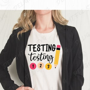 Peut inclure: Un t-shirt blanc avec le texte "TESTING testing 1 2 3" et un crayon jaune avec une gomme rose.