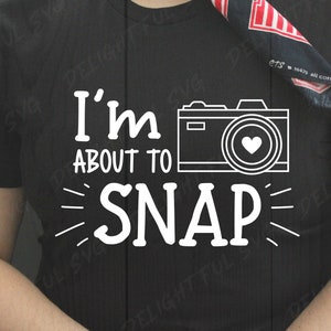 May include: Black t-shirt with white text that reads "I'm about to SNAP" and a white outline of a camera with a heart in the lens.