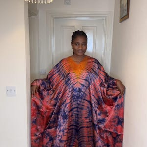May include: A vibrant, tie-dye caftan in shades of orange, red, and blue. The loose-fitting garment features a V-neck and wide sleeves. The fabric has a flowing drape, creating a comfortable and stylish look.